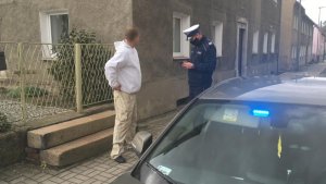 Policjant podczas legitymowania mężczyzny, przy nieoznakowanym radiowozie, na tle budynku mieszkalnego