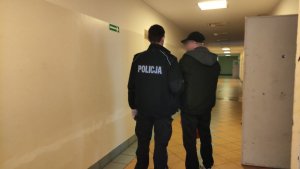 Na zdjęciu policjant prowadzący zatrzymanego