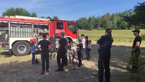 Na zdjęciu policjantka, strażak i dzieci na tle wozu strażackiego