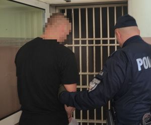 Na zdjęciu policjant z zatrzymanym przy kracie