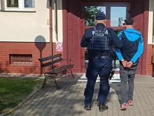 Na zdjęciu policjant prowadzi zatrzymanego
