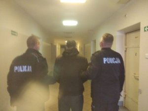 Dwóch umundurowanych policjantów prowadzi mężczyznę.