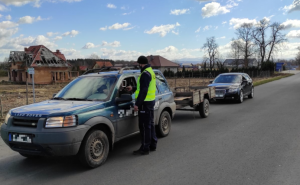 Na zdjęciu policjant podczas badania kierowcy na zawartość alkoholu. kierowca siedzi w pojeździe, za nim stoi kolejny samochód.