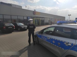 Na zdjęciu umundurowana policjantka przy radiowozie przed marketem