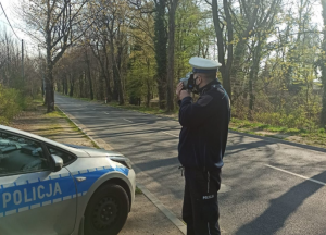 Na zdjęciu umundurowany policjant mierzący prędkość pojazdu