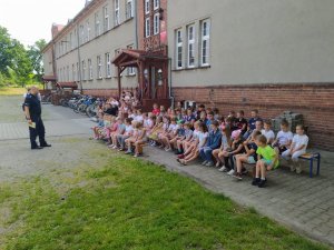 Na zdjęciu policjant tłumaczący uczniom zasady bezpiecznego wypoczynku nad wodą.