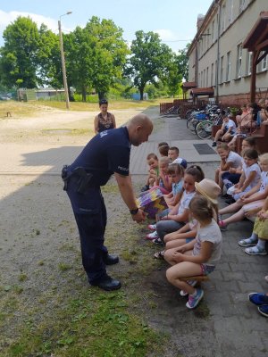 Na zdjęciu policjant wręczjący uczniom elementy odblaskowe.