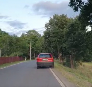 Na zdjęciu pojazd osobowy w kolorze czerwonym jadący poboczem