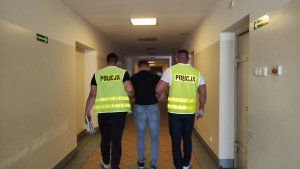 Na zdjęciu dwóch policjantów prowadzących zatrzymanego