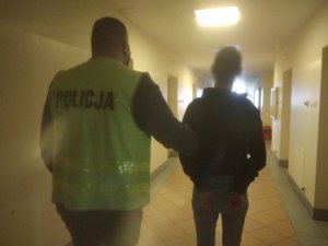 Na zdjęciu policjant prowadzący zatrzymanego