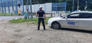 Na zdjęciu umundurowany policjant i radiowóz w tle przejazd kolejowy